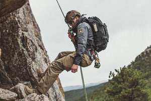 Man repelling and rock climbing down mountain with black backpack