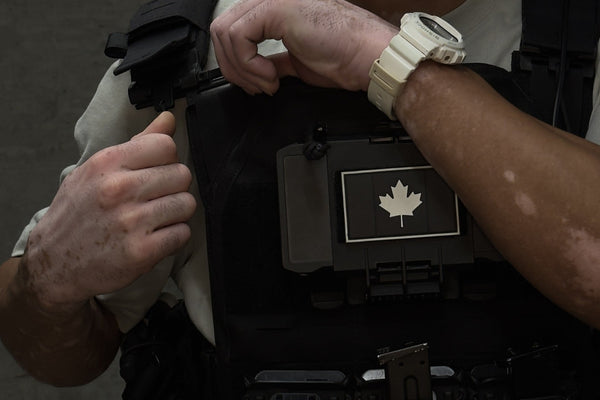 Person wearing a tactical vest with a maple leaf emblem on a dark background